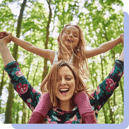 Mother carrying child on her shoulders amongst trees