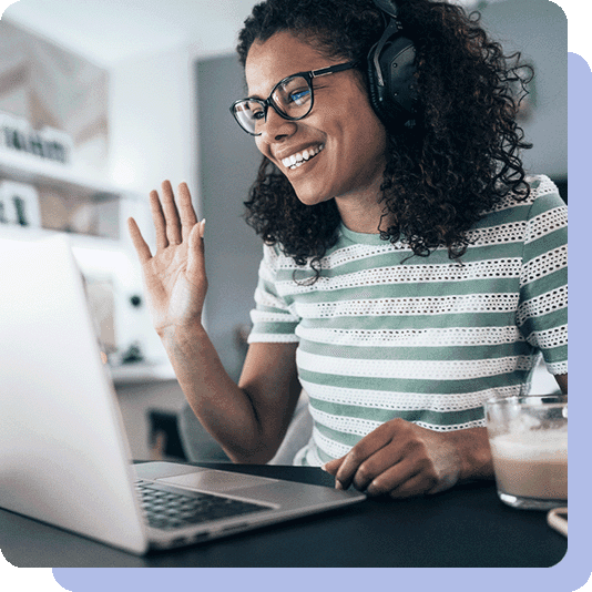 Woman sat at laptop, wearing headphones, and waving