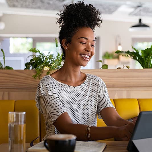 Woman smiling, working at a laptop in a coffee shop