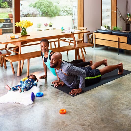 Father and mother practising yoga in their home with a baby lying near them