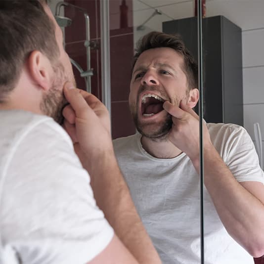 Man examining his mouth in the mirror