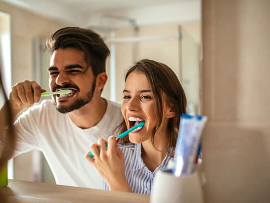 Man and woman brushing teeth together in front of mirror