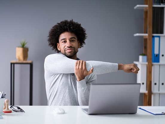 Man sat at laptop and stretching his arm