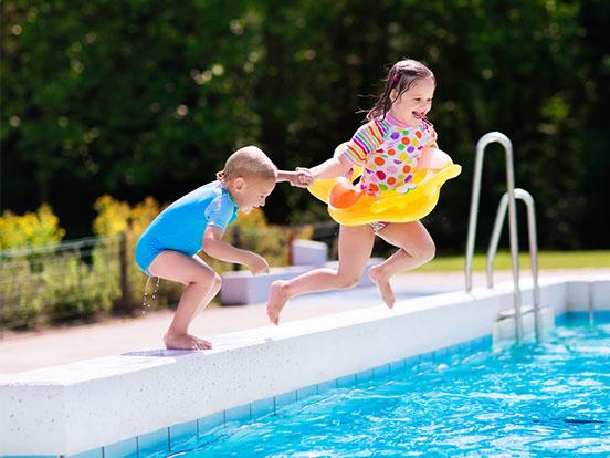 Two young children jumping into an outdoor pool