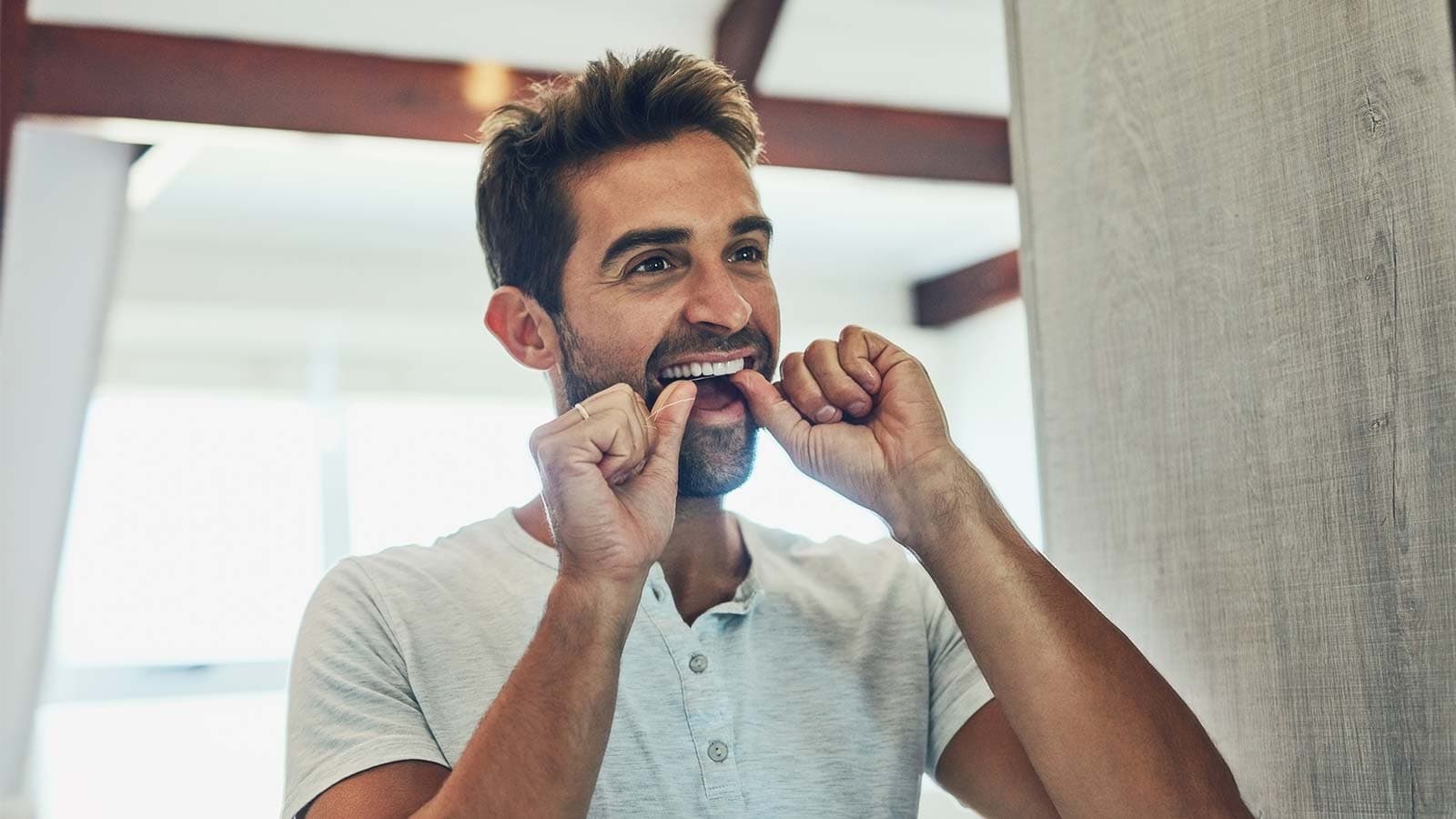 Man flossing his teeth in mirror