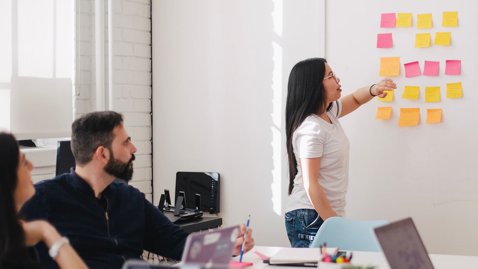A woman looking at sticky notes on a wall in front of colleagues