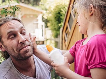 Dad and daughter putting on sun cream in garden