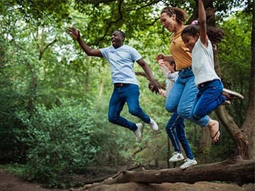 Family playing in the forest jumping off log