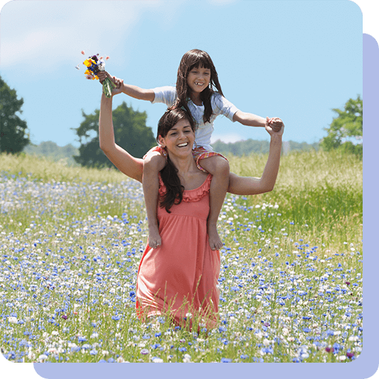 Mum with daughter on shoulders walking in a meadow