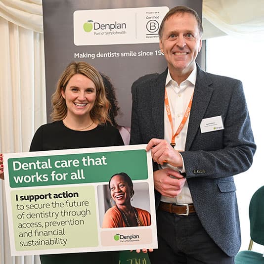 Two people smiling, holding a sign promoting dental care accessibility and sustainability