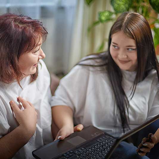Mother and daughter having chat on sofa with laptop