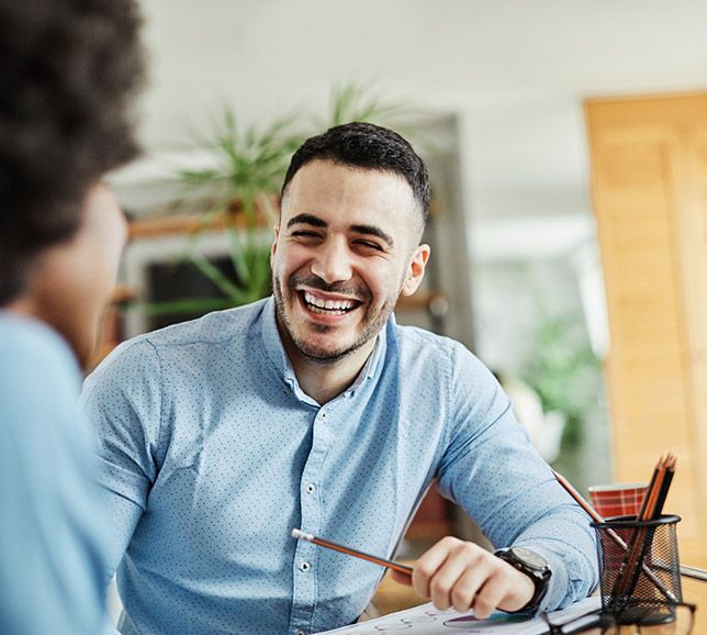 Man sat with colleague at a desk and smiling