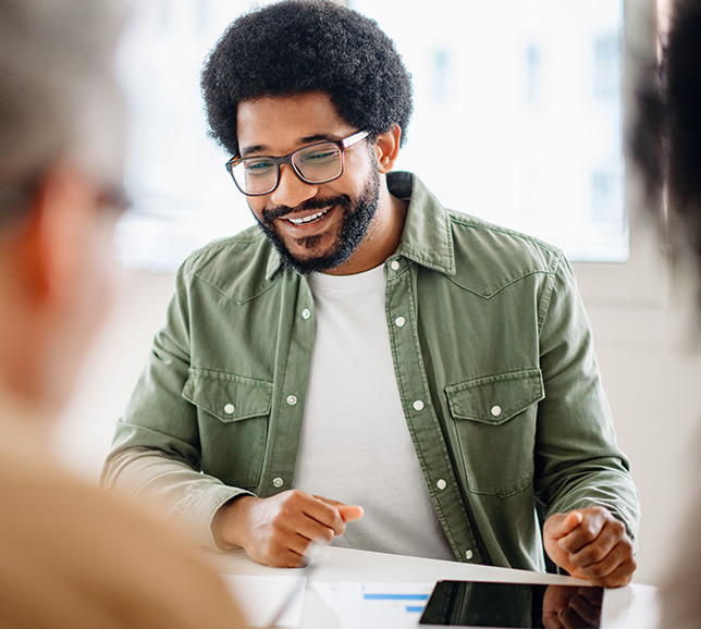 Man wearing glasses and a green shirt, sat at desk with colleagues